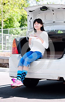 Preteen girl sitting on back car bumper eating lunch