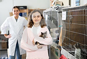 Preteen girl standing in animal shelter with kitten in hands