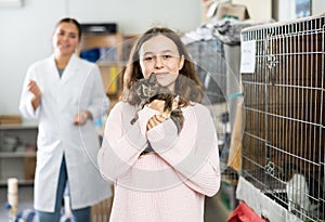 Preteen girl standing in animal shelter with kitten in hands