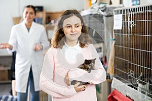 Preteen girl standing in animal shelter with kitten in hands