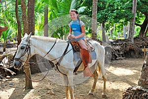 Preteen girl on a white horse in the tropics