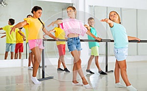 Preteen girls practicing ballet positions near bar in choreographic school