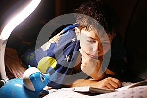 Preteen handsome boy read book with lamp before sleep