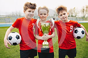 Preteen happy soccer players after final game. Boys holding golden cup and soccer balls