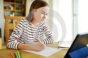 Smart preteen schoolgirl doing her homework with digital tablet at home. Education and distance learning for kids. Homeschooling photo