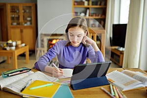 Preteen schoolgirl doing her homework with digital tablet at home. Child using gadgets to study. Education and distance learning