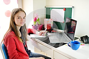 Preteen schoolgirl doing her homework with laptop computer at home. Child using gadgets to study. Online education and distance