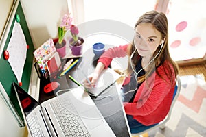 Preteen schoolgirl doing her homework with laptop computer at home. Child using gadgets to study. Online education and distance