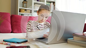 Preteen schoolgirl doing her homework with laptop computer at home. Child using gadgets to study. Online education and distance