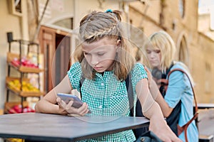 Preteen schoolgirl and teenage student with backpacks using smartphones, outdoor