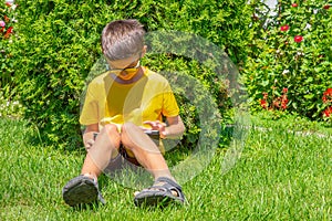 Preteenage Boy reading ebook on a gren grass