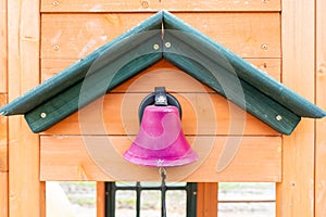 Pretend pink school bell on a wooden playground outdoors, with a string for making the ding dong noise, while kids participate in