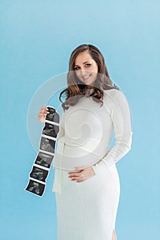 Pretty 20-week pregnant woman with ultrasound scan image on blue background