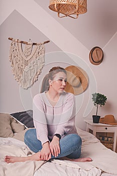 Pretty 25-year-old girl at home on  bed in  sweater and jeans