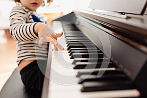 Pretty 3-year-old girl plays the keys of a piano and reads the sheet music with difficulty