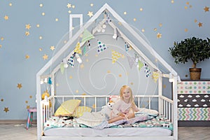 Pretty 3-year-old girl sitting in cute house bed