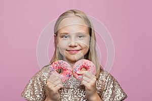 Pretty adorable kid girl holding donut and having fun against pink color studio wall background. Colorful holiday birthday party