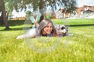 Pretty adult caucasian happy woman resting in the park on a sunny day with her beloved dog. Female lies on the grass, smiling and
