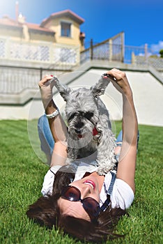 Pretty adult caucasian happy woman resting in the park on a sunny day with her beloved dog. Female lies on the grass, smiling and