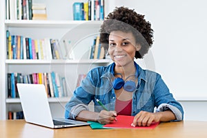 Pretty african american female student learning at desk indoors at library