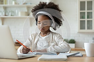 Pretty African American little girl wearing headphones studying at home