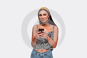 Pretty african-american woman in a headband, sleeveless t-shirt and jeans holding smartphone and looking at the camera.