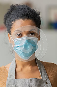 Pretty African American woman in medical mask. Young female mixed race posing in an apron against the backdrop of a