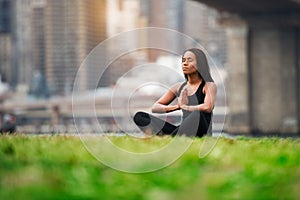 Pretty african american woman sitting on green grass doing yoga in New York City park