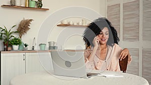 Pretty African American woman studying online or working remote using laptop and talking on mobile phone. Black female