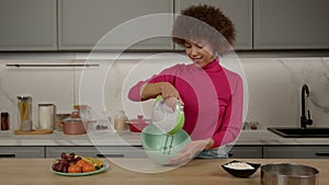 Pretty African American woman whisking eggs in bowl with handheld mixer