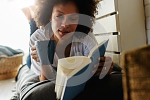 Pretty african american young woman reading a book at home