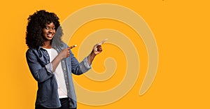 Pretty african woman pointing at copy space on yellow