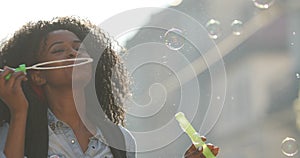 The pretty afro-american girl with curly hair is blowing the soap bubbles and spinning round during the walk in the