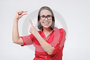 Pretty amazed woman in red shirt and glasses shows something invisible with her fingers