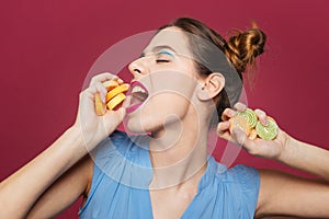 Pretty amusing young woman holding and eating fruit jelly candies