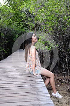 Pretty Asain girl is smiling and sitting on wooden bridge in the tropical mangrove forest at Thailand