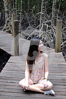 Pretty Asain girl is smiling and sitting on wooden bridge in the tropical mangrove forest at Thailand
