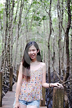 Pretty Asain girl is smiling and standing on wooden bridge in the tropical mangrove forest at Thailand