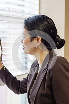 Pretty asian businesswoman looking through office window blinds