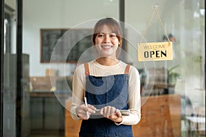 A pretty Asian female coffee shop owner in an apron standing at the entrance door