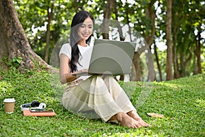 Pretty Asian female college student doing an online homework on her laptop in the city park