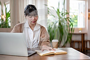 A pretty Asian female college student focuses on her work while sitting at a table in a coffee shop