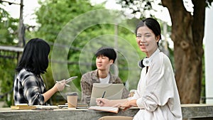 A pretty Asian female college student sits at a table in the campus park with her friends