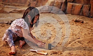 A young Asian girl playing in a sandbox with a modeled dinosaur fossil using brush and shovel photo