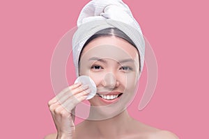 Pretty asian girl in a white headscarf cleaning her face with a sponge and feeling happy