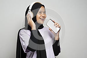 Pretty Asian muslim girl using headphone for listen music by smartphone and singing using her phone as a microphone