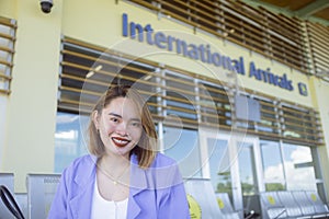 A pretty asian traveler or tourist in a lavender blazer in front of the International arrivals area of an airport
