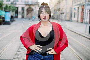 Pretty Asian woman with black ponytail hair wearing stylish casual red jacket, black top and jeans, standing on the city
