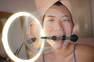 Pretty Asian woman brushing her face - lifestyle portrait of young happy and beautiful Japanese girl at home applying makeup and