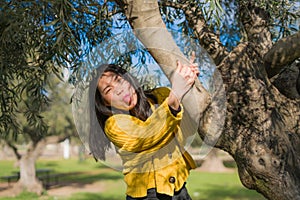 Pretty Asian woman in city park - lifestyle portrait of young beautiful and happy Chinese girl playful by a tree enjoying enjoying